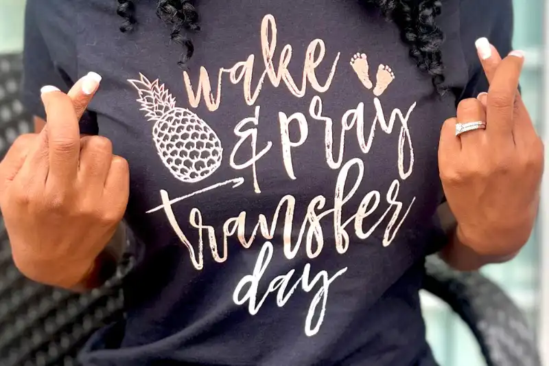 A real surrogate wearing a fun transfer day themed t-shirt that says “wake & pray, transfer day”. She is crossing her fingers.