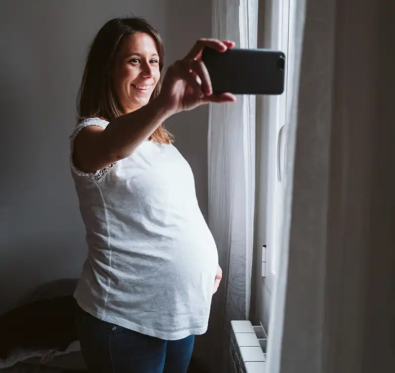 A pregnant woman taking a selfie while smiling